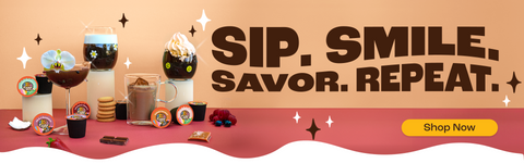 An image of multiple coffee drinks, some with whipped cream or milk foam, with various crazy cup pods and flavor elements such as chocolates, berries, caramels, and cookies, with the title "Sip, smile, savor, repeat." and a yellow shop now button.